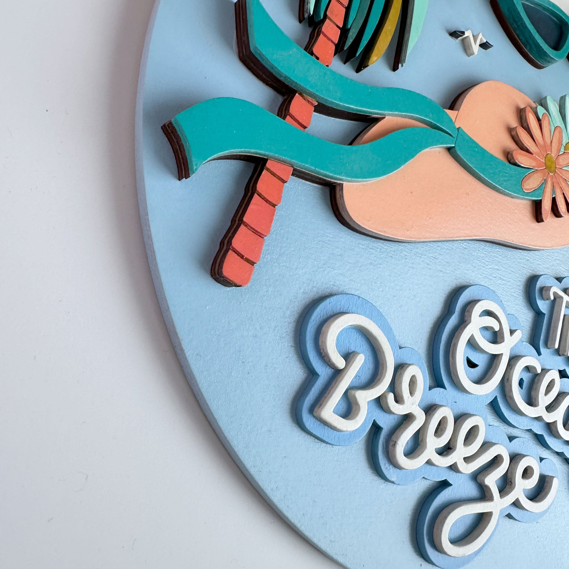 Decorative wall art with palm tree, beach ball, and 'The Ocean Breeze' text on a light blue background.