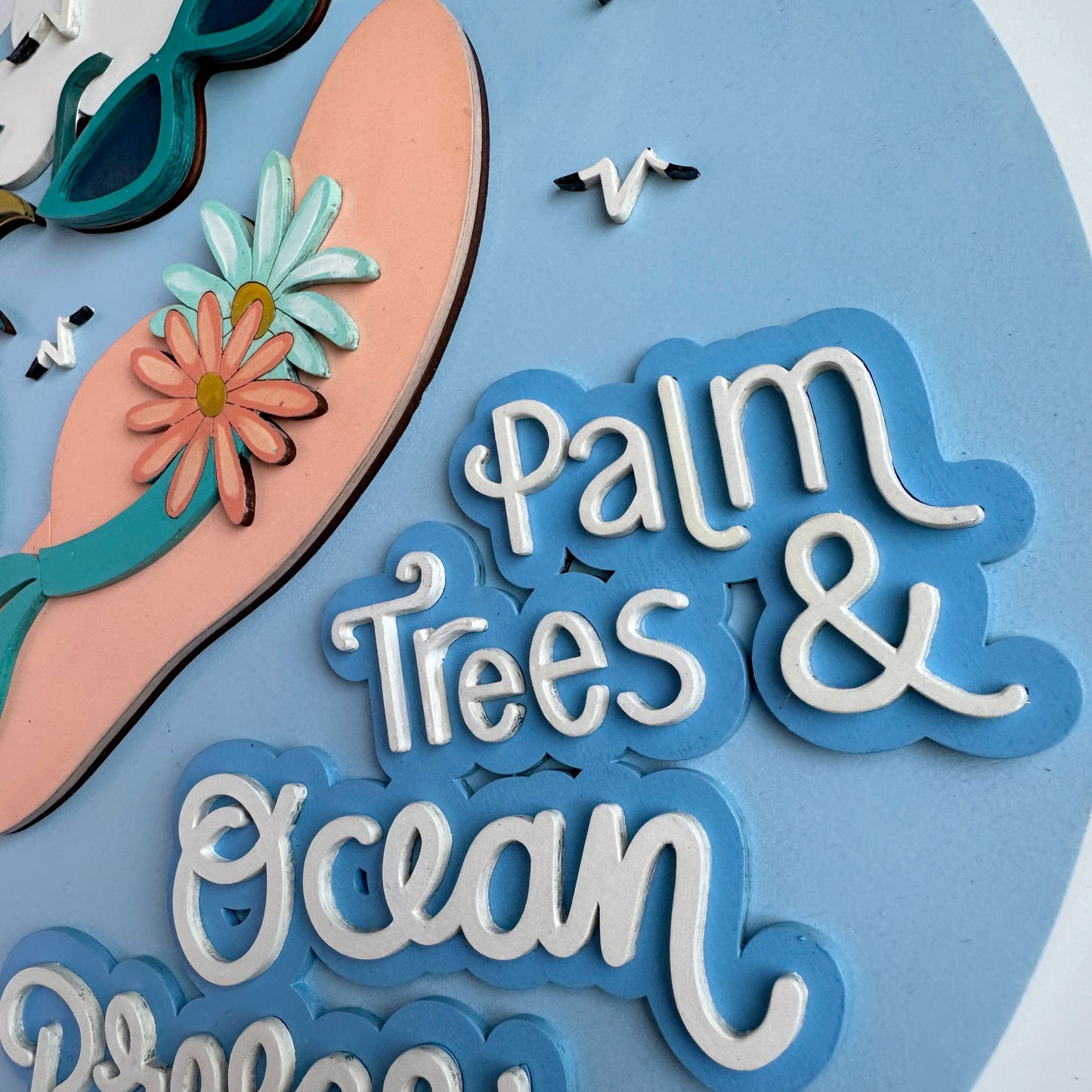 Decorative cutout with 'Palm Trees & Ocean Breeze' text, sunglasses, and a sandal on a blue background.