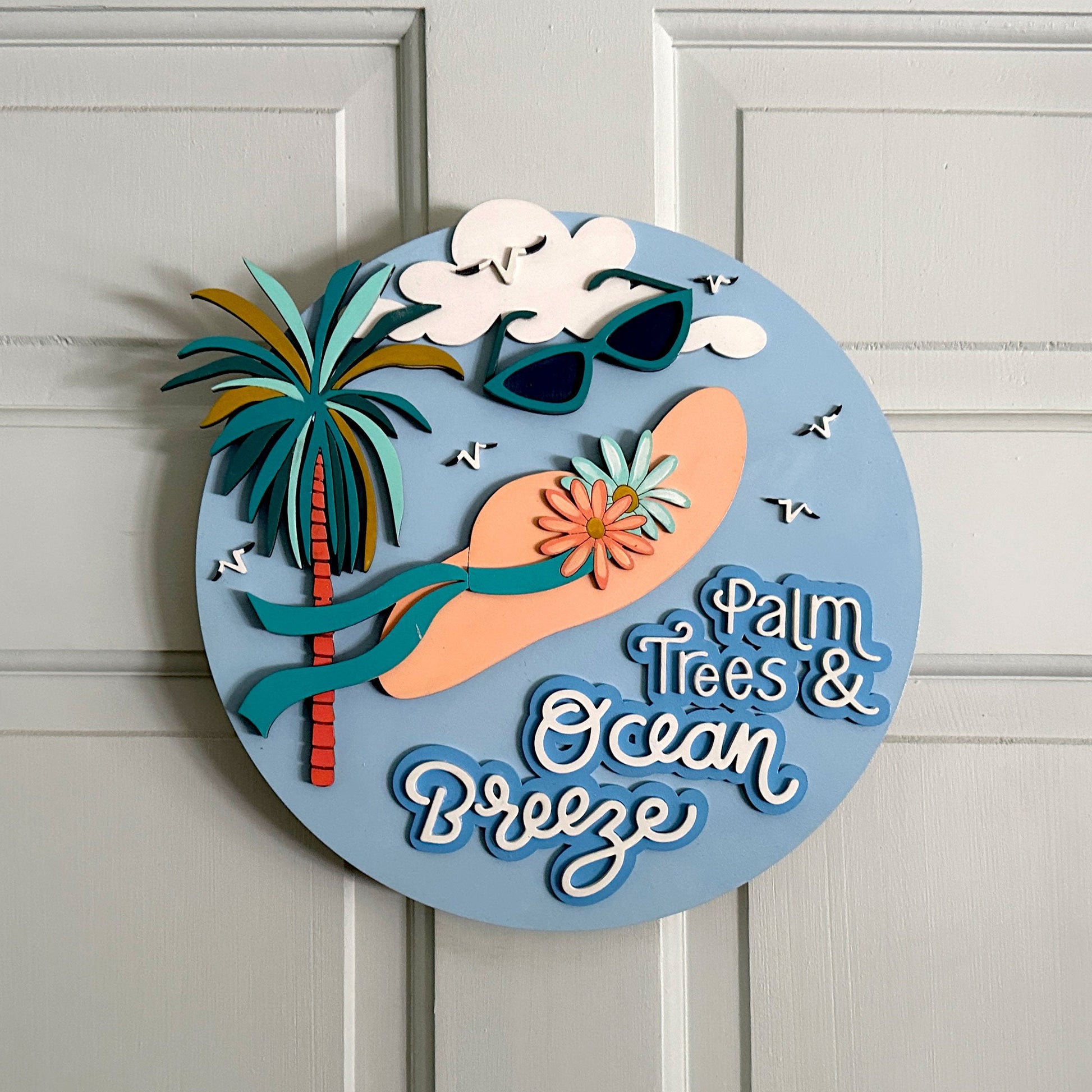 Decorative sign with palm trees, sunglasses, and 'Palm Trees & Ocean Breeze' text on a white door.
