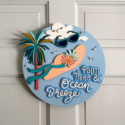 Decorative sign with palm trees, sunglasses, and 'Palm Trees & Ocean Breeze' text on a white door.