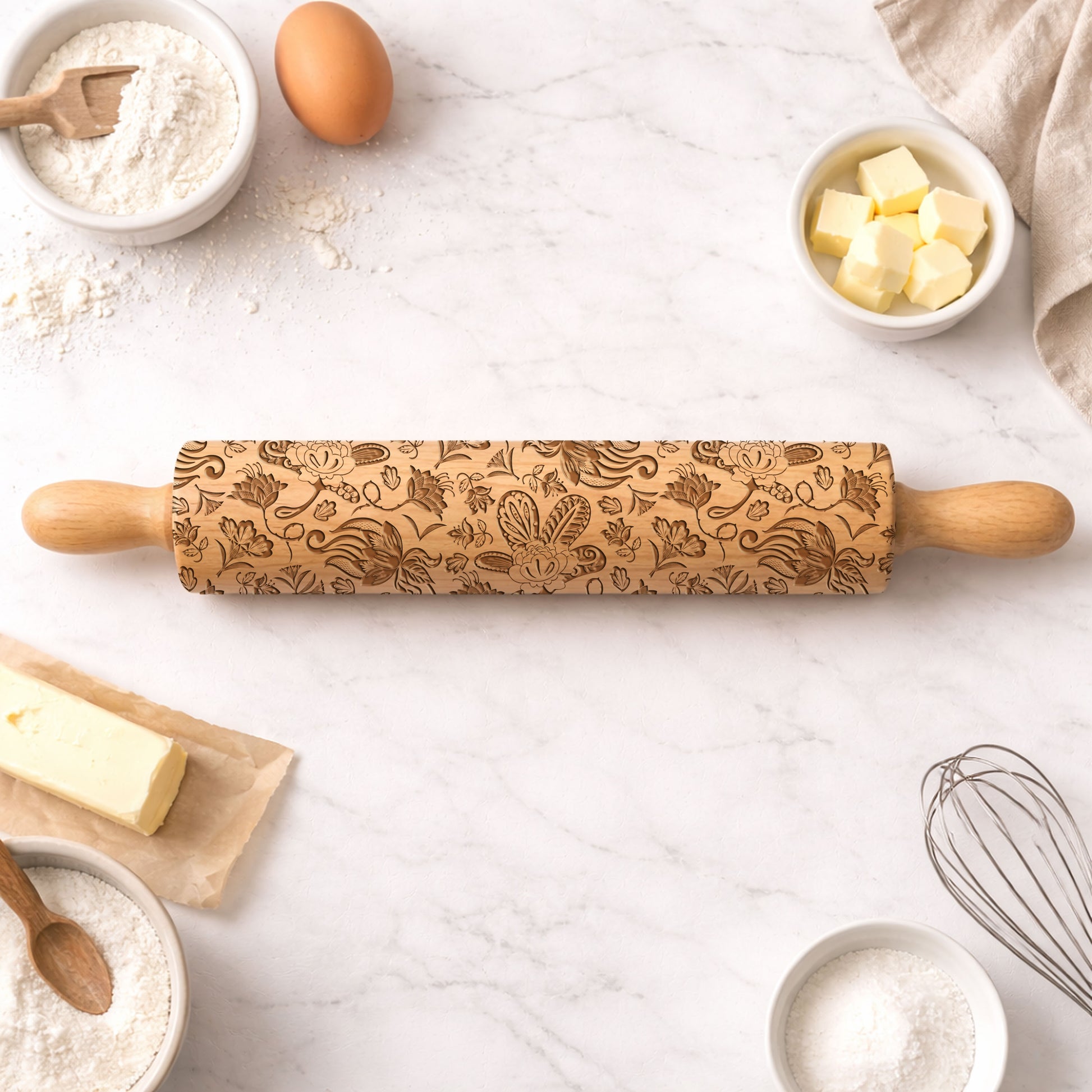 Decorative rolling pin with floral patterns on a kitchen counter with baking ingredients.