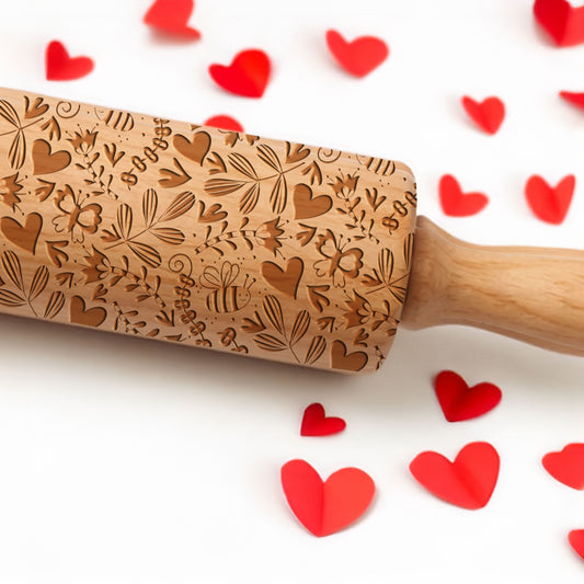 Wooden embossing rolling pin with heart patterns on a white background with red heart shapes.
