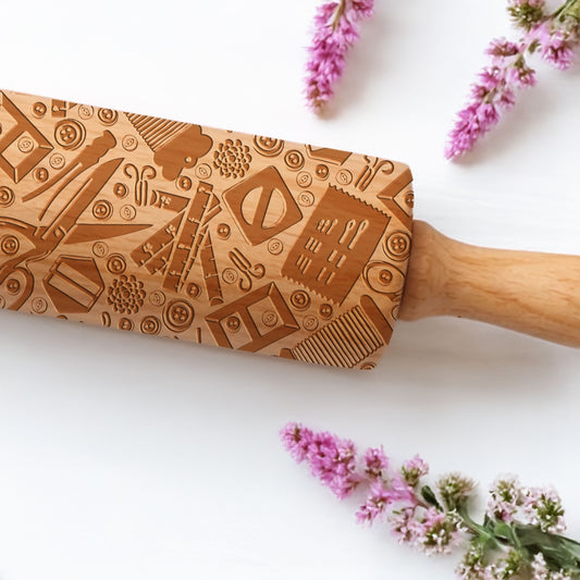 Wooden rolling pin with engraved designs on a white background with pink flowers.