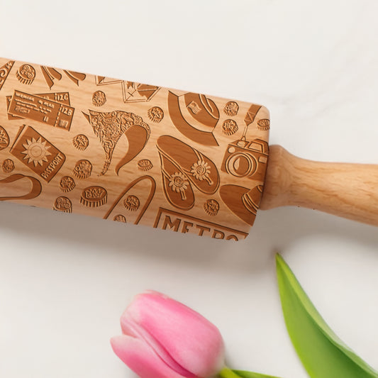 Wooden rolling pin with engraved patterns on a white background with a pink tulip.