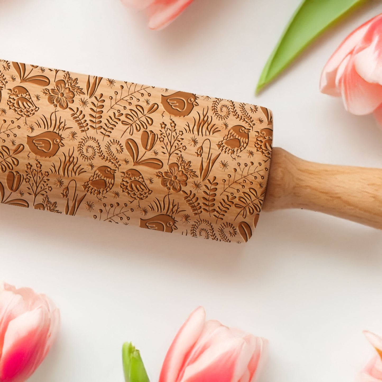Wooden rolling pin with floral patterns on a white surface with tulips.
