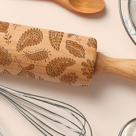 Wooden rolling pin with paisley patterns on a kitchen counter with utensils.
