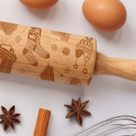 Wooden rolling pin with embossed patterns on a white surface with eggs, star anise, cinnamon stick, and whisk.