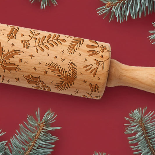 Wooden rolling pin with engraved patterns on a red background with pine branches.
