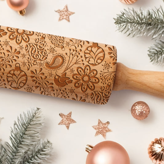 Wooden rolling pin with floral patterns on a white surface with Christmas decorations.