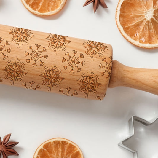 Wooden rolling pin with engraved patterns on a white surface with oranges and star anise.