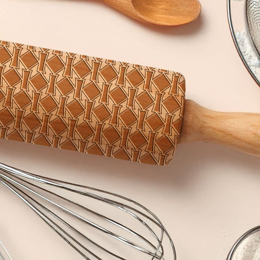 Wooden rolling pin with a patterned handle on a kitchen counter with utensils.