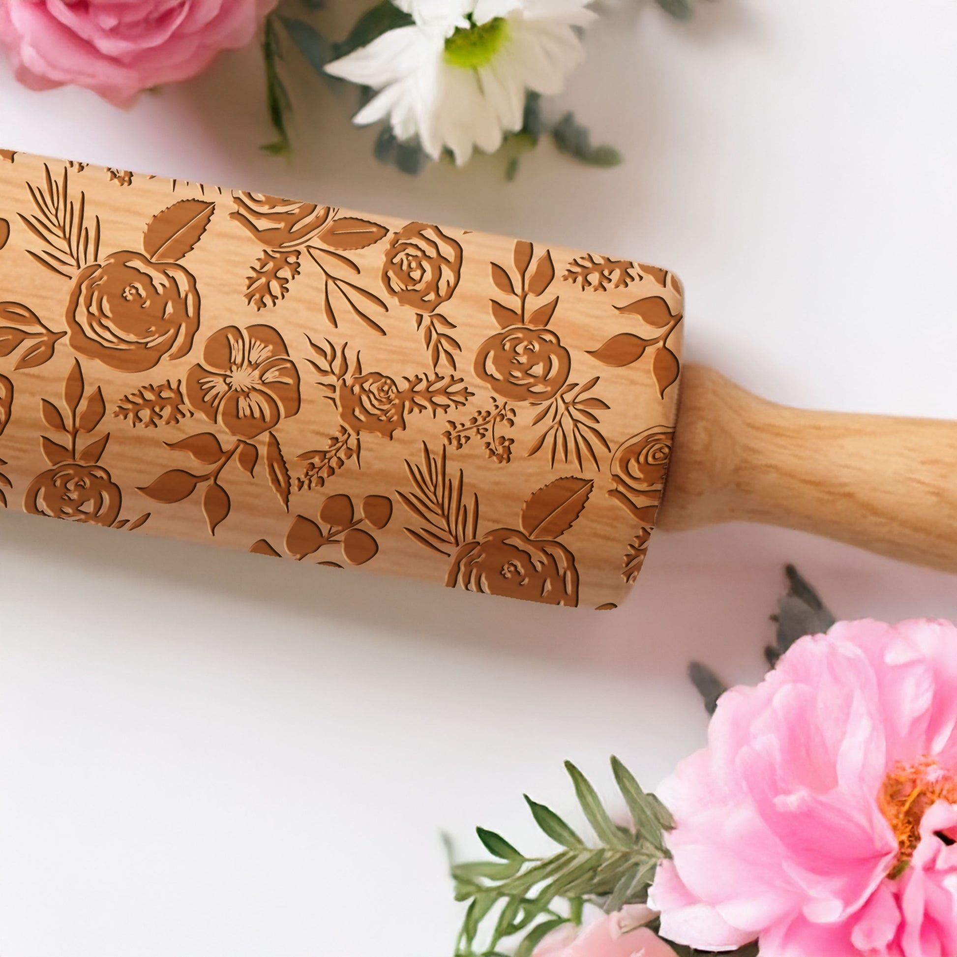 Wooden rolling pin with floral patterns on a white surface with flowers around