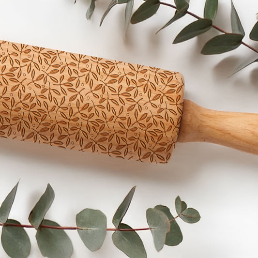 Wooden rolling pin with leaf pattern on a white background with eucalyptus leaves.