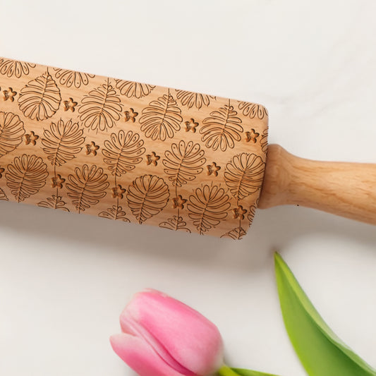 Wooden rolling pin with leaf patterns on a white background with a pink tulip and green leaf.