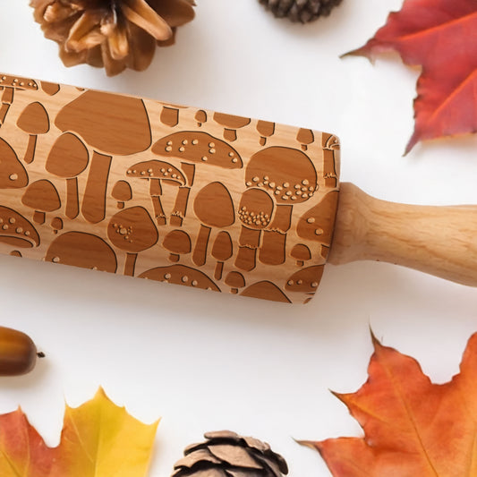 Wooden rolling pin with mushroom pattern on a white background with autumn leaves and pinecones.