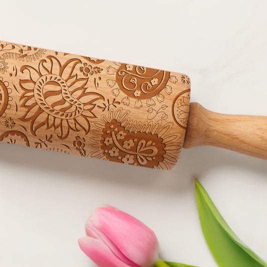 Wooden rolling pin with floral patterns on a white background with a pink tulip and green leaf.
