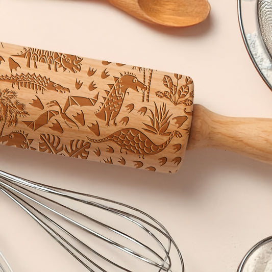 Wooden rolling pin with dinosaur patterns on a kitchen counter with utensils.