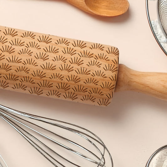 Wooden rolling pin with decorative pattern on a light surface with kitchen utensils.