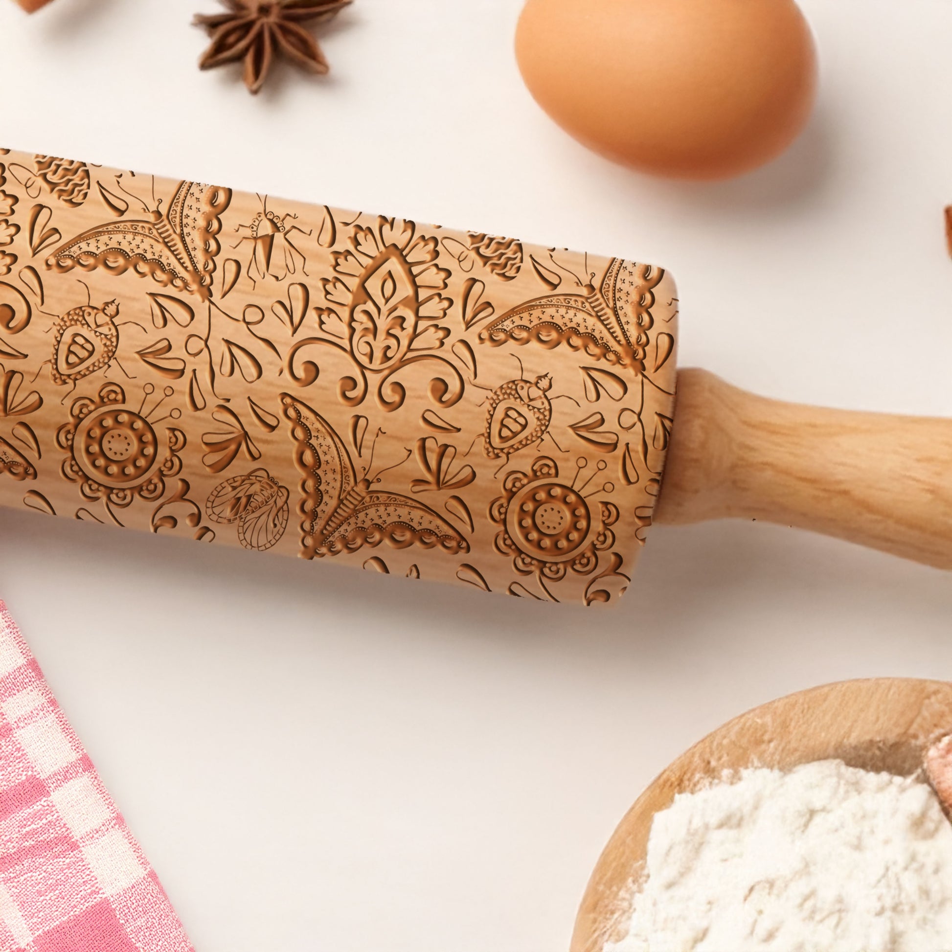 Decorative wooden rolling pin with intricate patterns on a kitchen counter with flour and eggs.