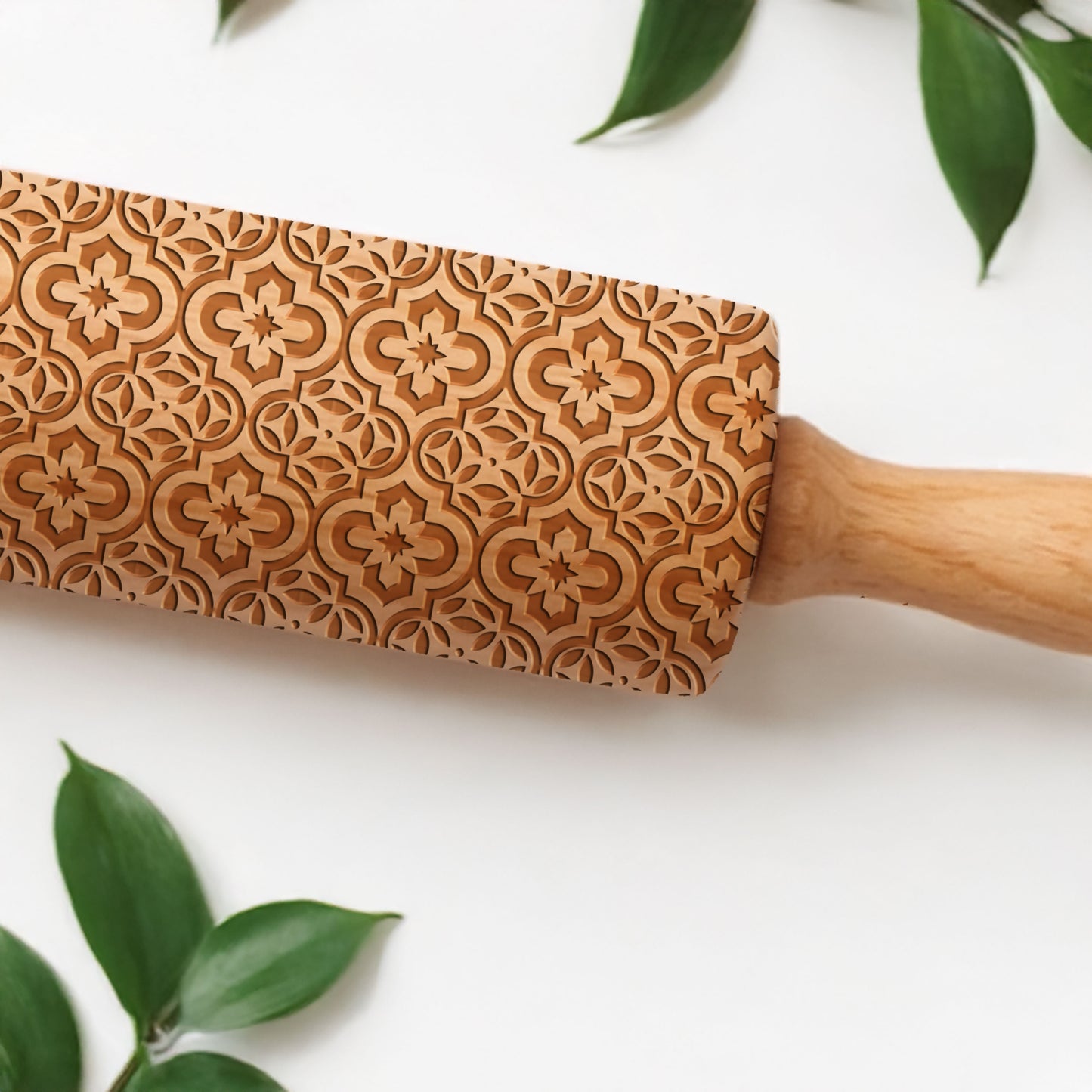 Wooden rolling pin with intricate floral patterns on a white background with green leaves.