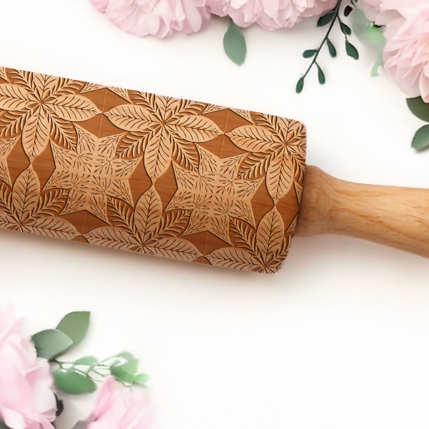 Wooden rolling pin with leaf pattern on a white background with pink flowers and green leaves.