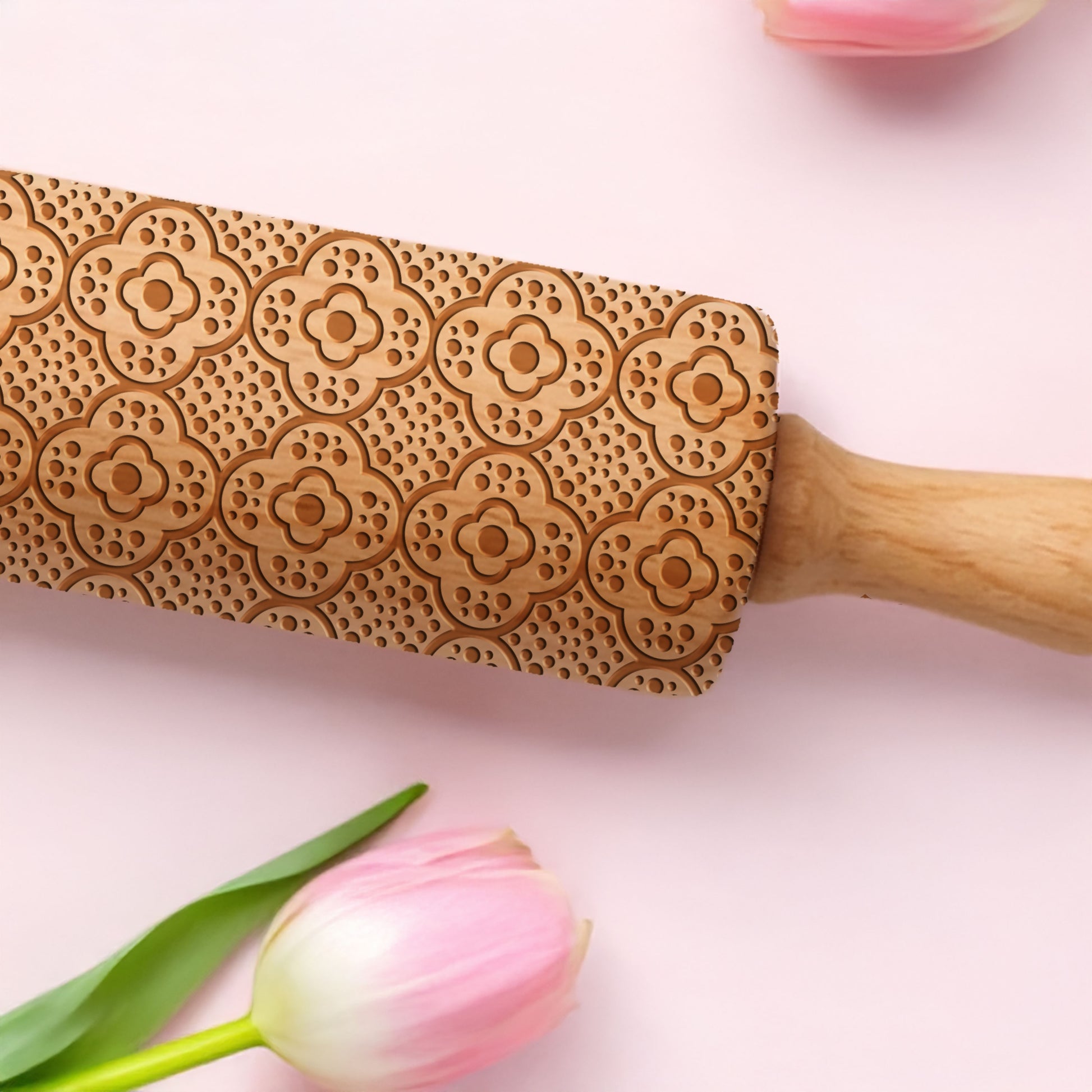 Wooden embossing rolling pin with floral patterns on a pink background with tulips.