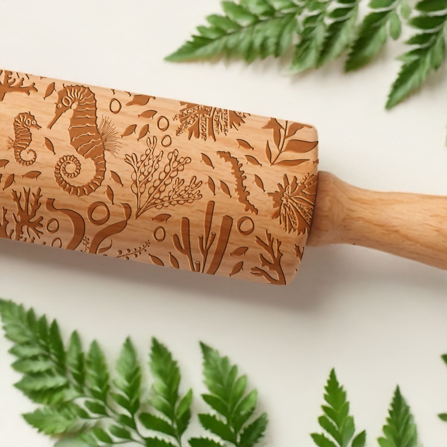 Wooden rolling pin with engraved seahorse and plant designs on a white background with green leaves.