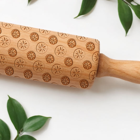 Wooden rolling pin with engraved patterns on a white background with green leaves.