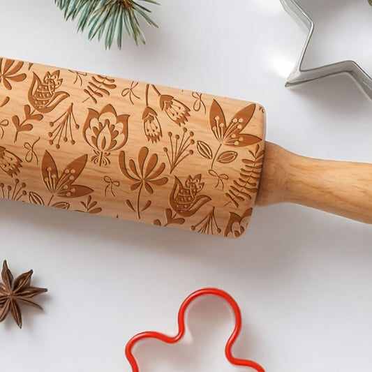Wooden rolling pin with floral patterns on a white surface with cookie cutters and spices.