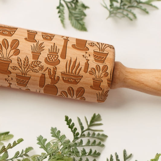 Wooden rolling pin with plant patterns on a white background with greenery.