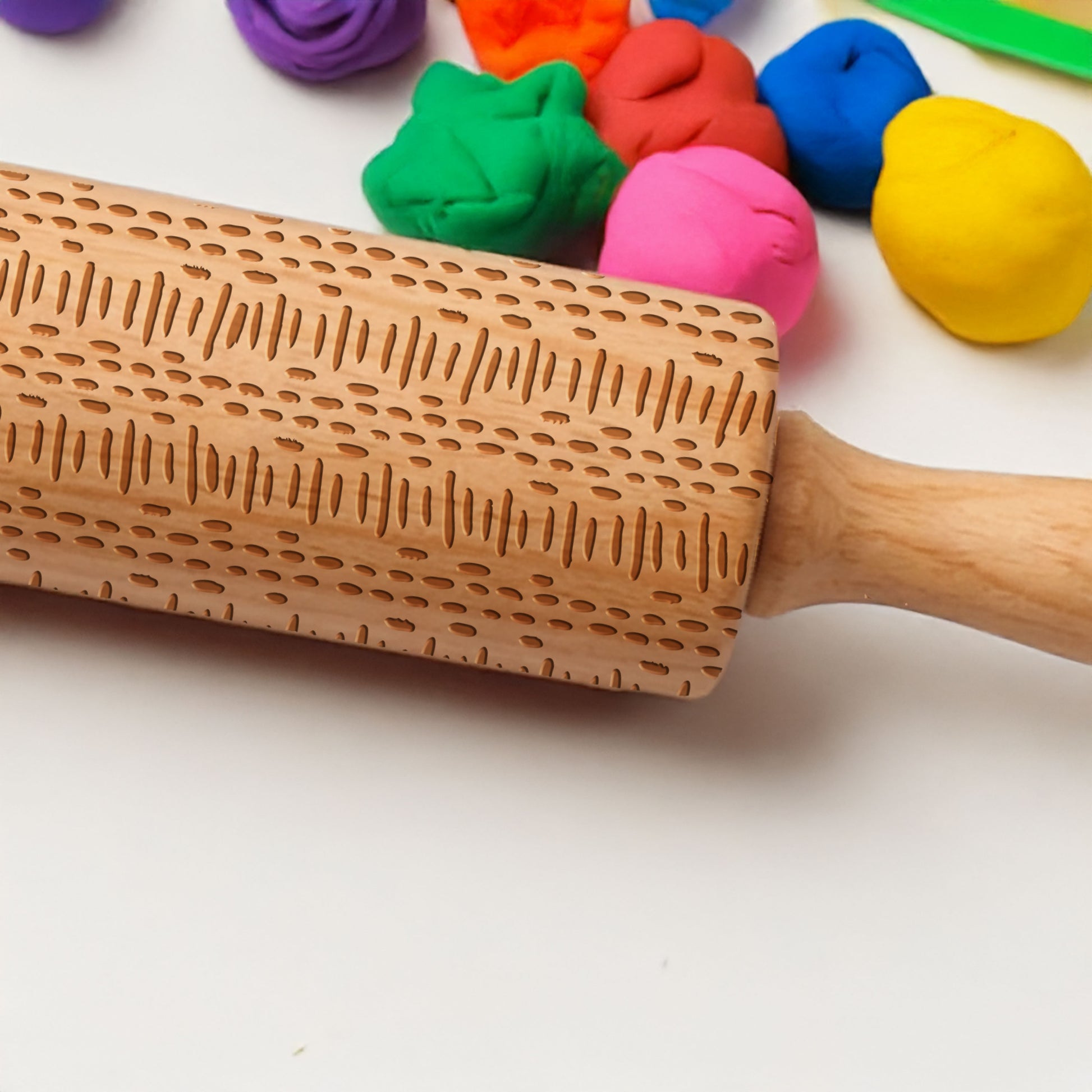 Wooden rolling pin with engraved pattern on a white background with colorful play dough.