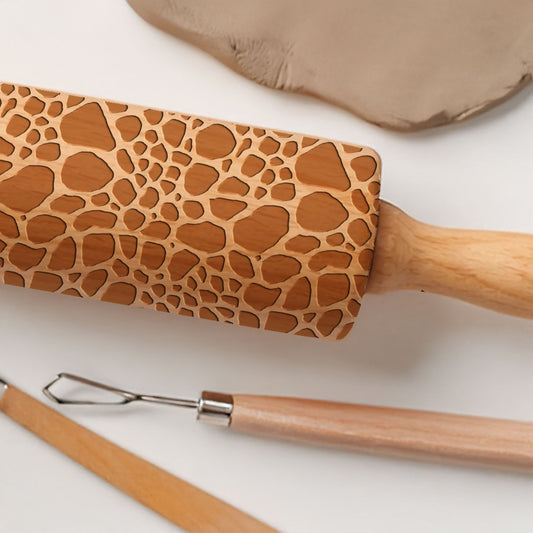 Rolling pin with giraffe pattern on a white background with a slab of clay and clay tools.