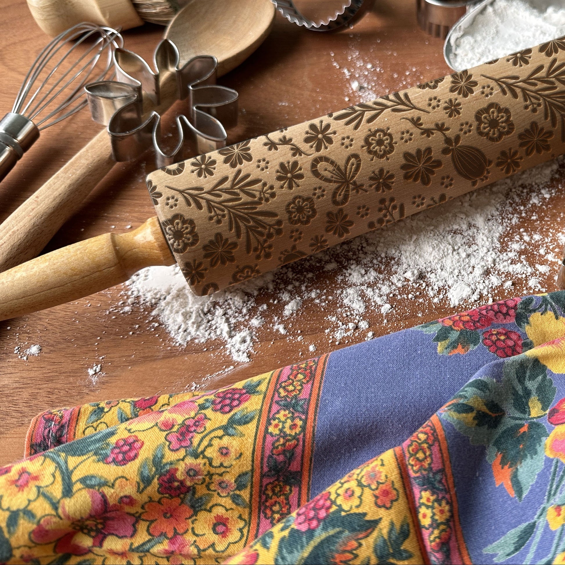 Decorative rolling pin with floral patterns on a wooden surface with baking tools and flour.