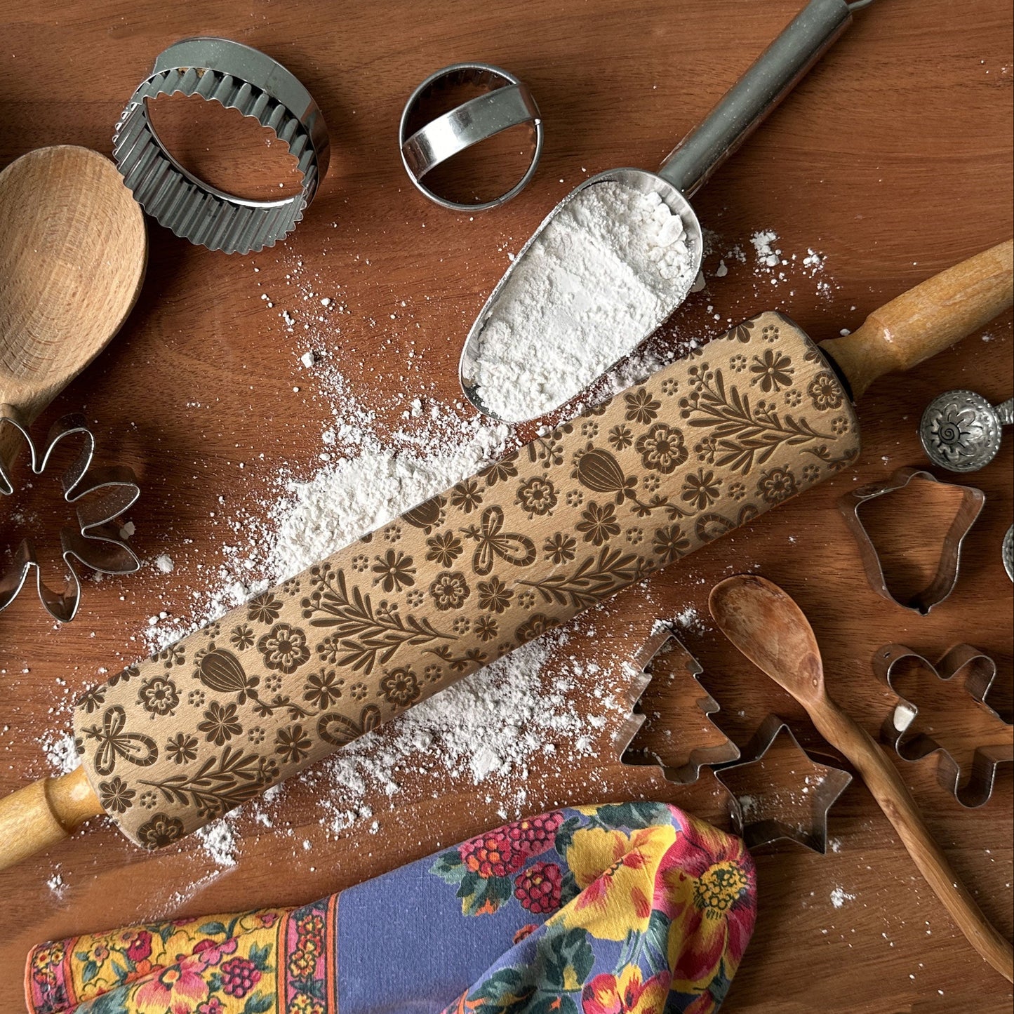 Decorative rolling pin with floral patterns on a wooden surface with flour and baking tools.