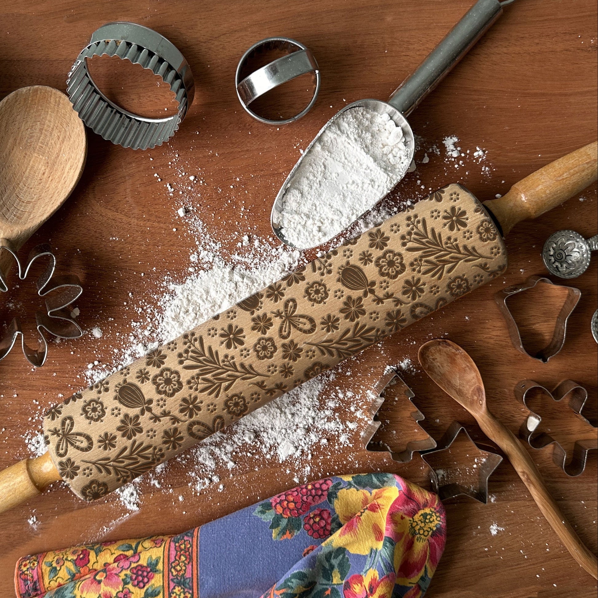 Decorative rolling pin with floral patterns on a wooden surface with flour and baking tools.