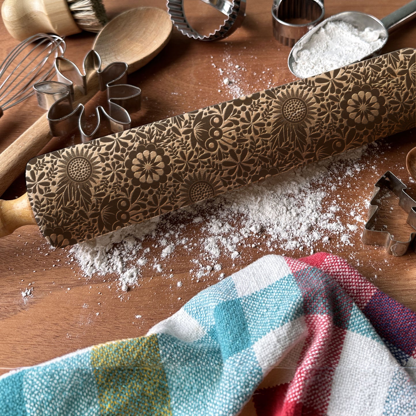 Decorative rolling pin with floral patterns on a wooden surface with flour and kitchen tools.