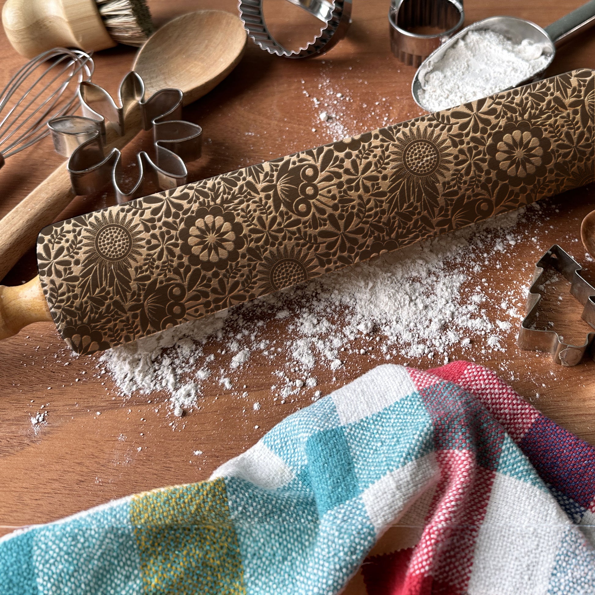 Decorative rolling pin with floral patterns on a wooden surface with flour and kitchen tools.