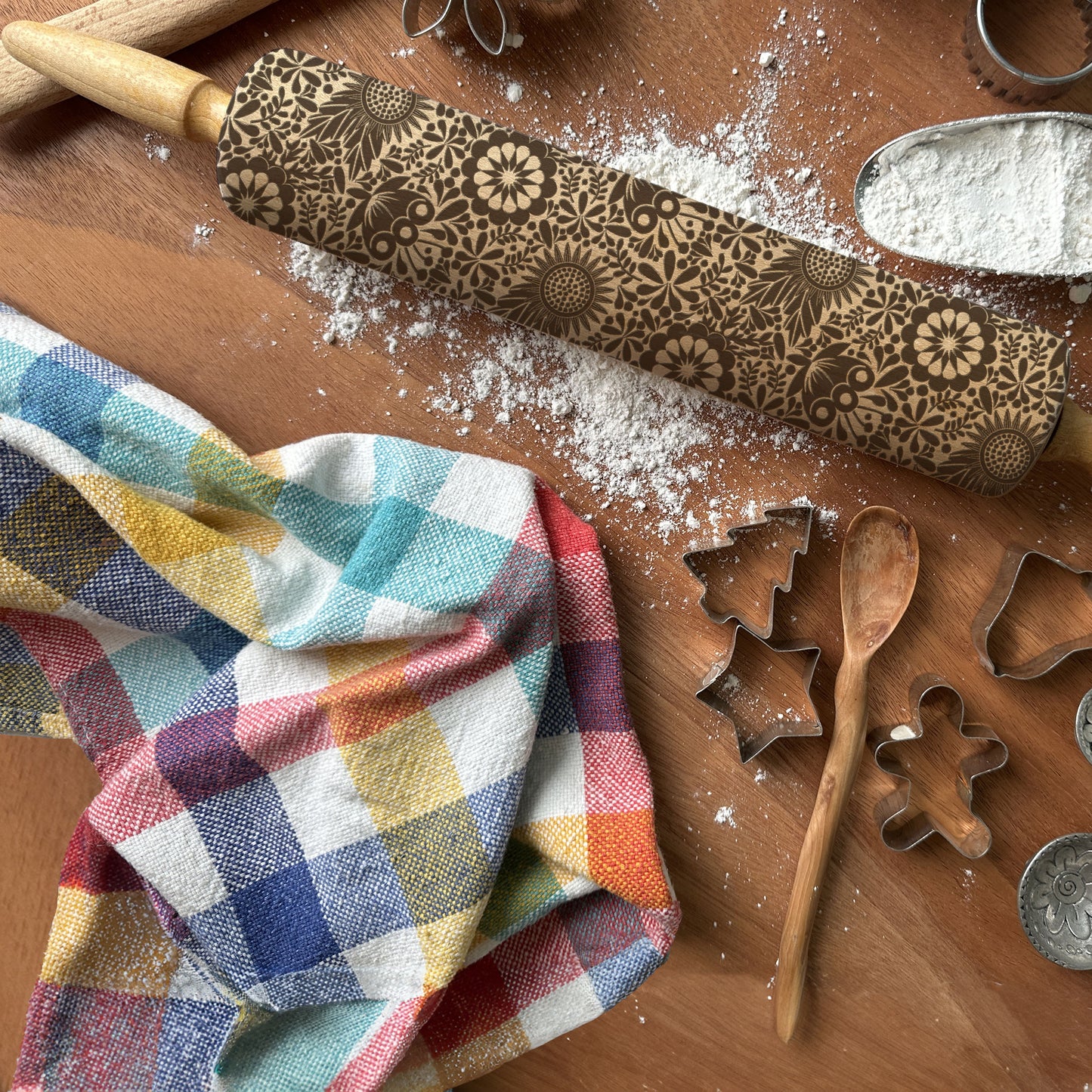 Decorative rolling pin with floral patterns on a wooden surface with baking tools and flour.