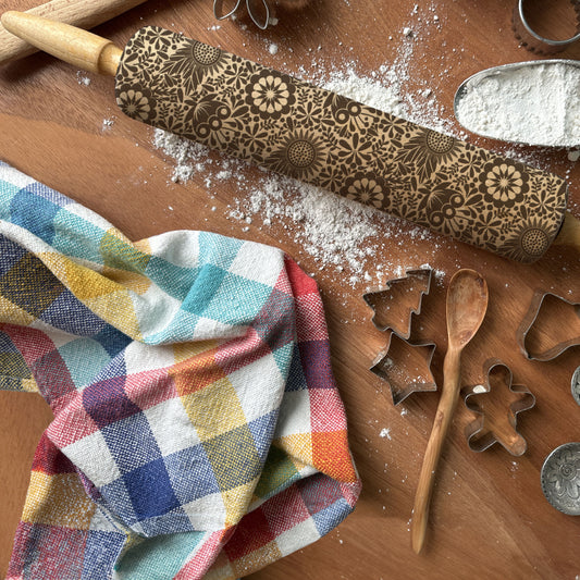 Decorative rolling pin with floral patterns on a wooden surface with baking tools and flour.