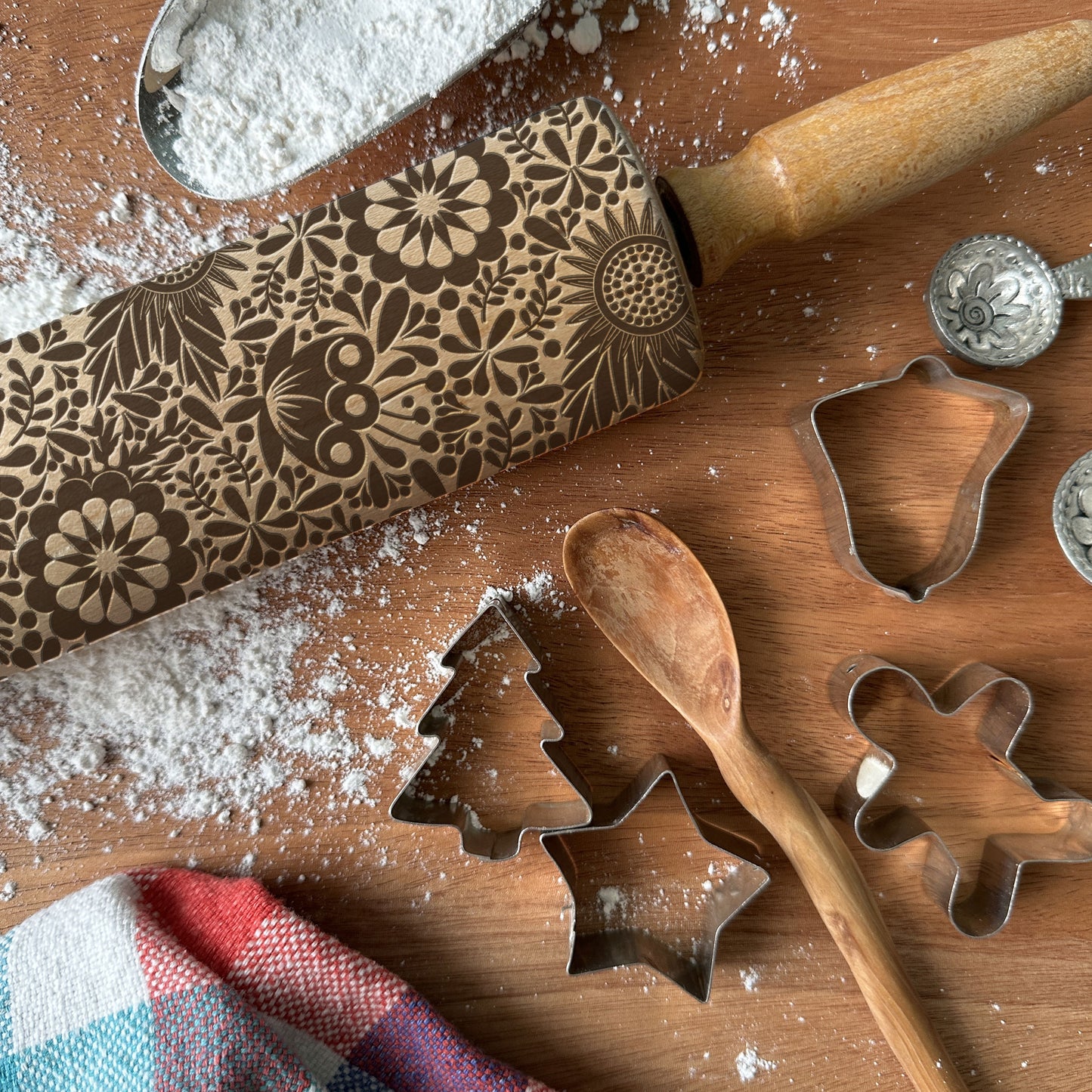 Wooden rolling pin with floral patterns and metal cookie cutters on a wooden surface with flour.