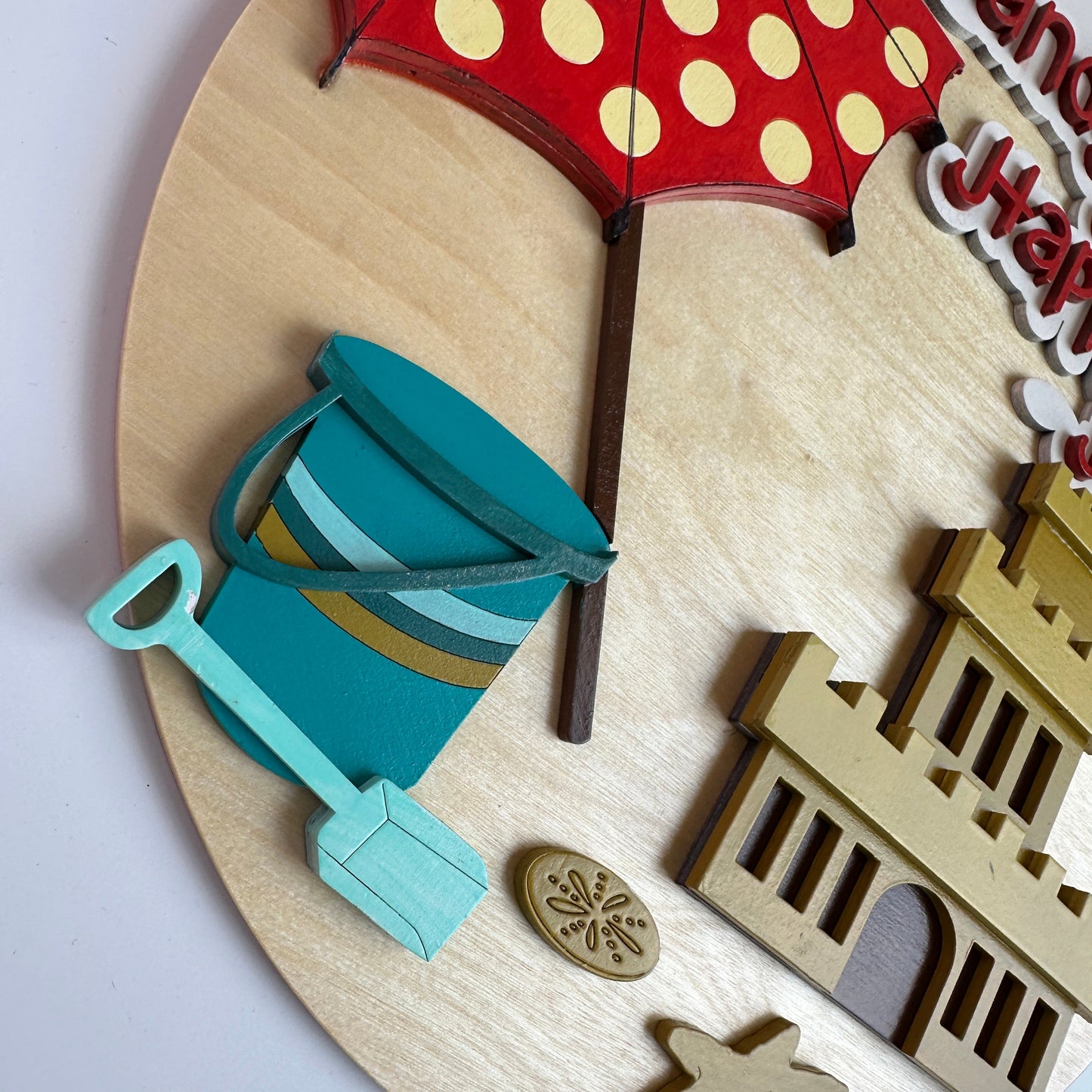 Wooden wall decor with beach-themed elements including a red umbrella with white polka dots, blue bucket, and sandcastle.