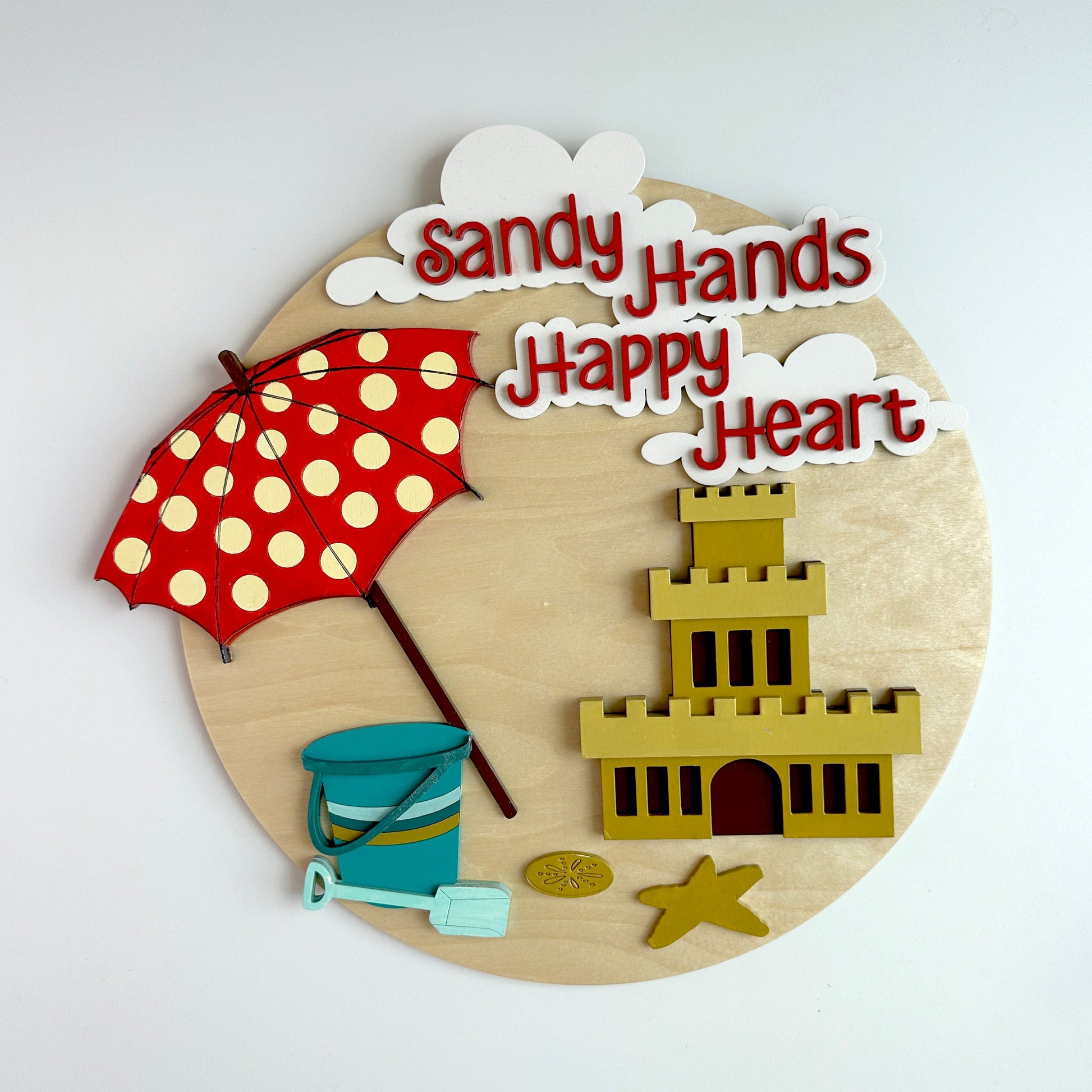 Decorative wall piece with beach-themed elements and 'Sandy Hands Happy Heart' text on a light background.