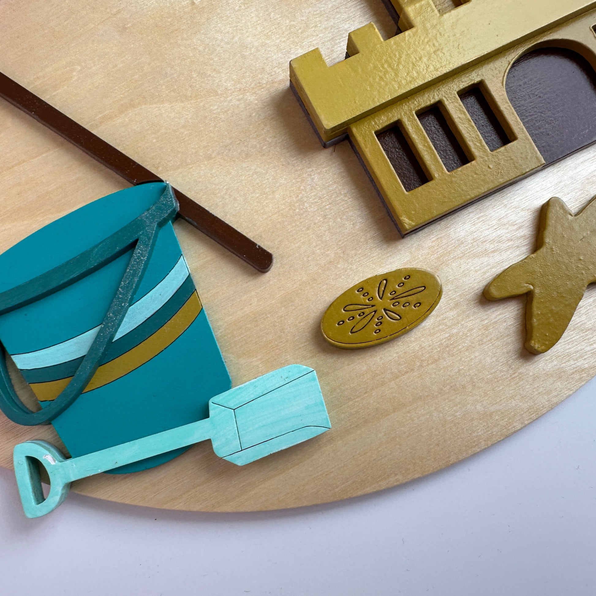 Children's sand toys including a bucket and shovel on a wooden surface with decorative elements.