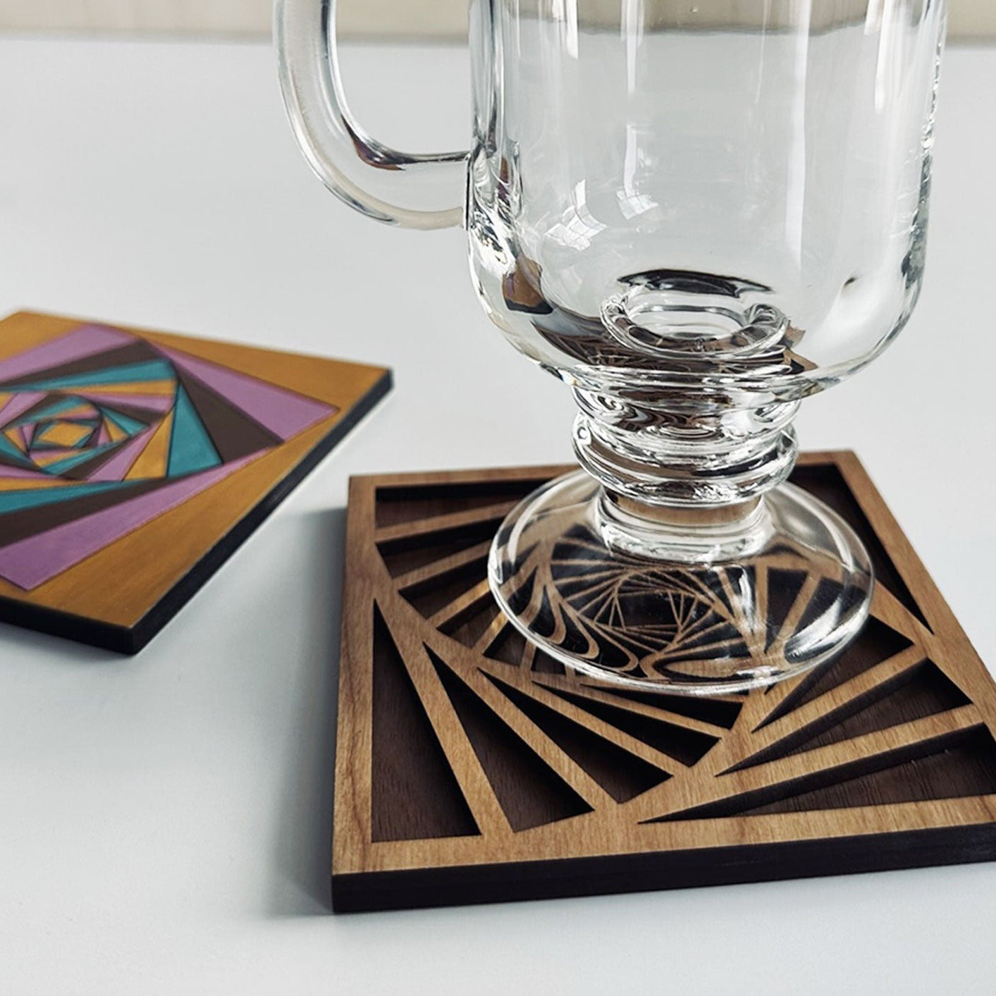 Clear glass mug on a geometric wooden coaster with a white background