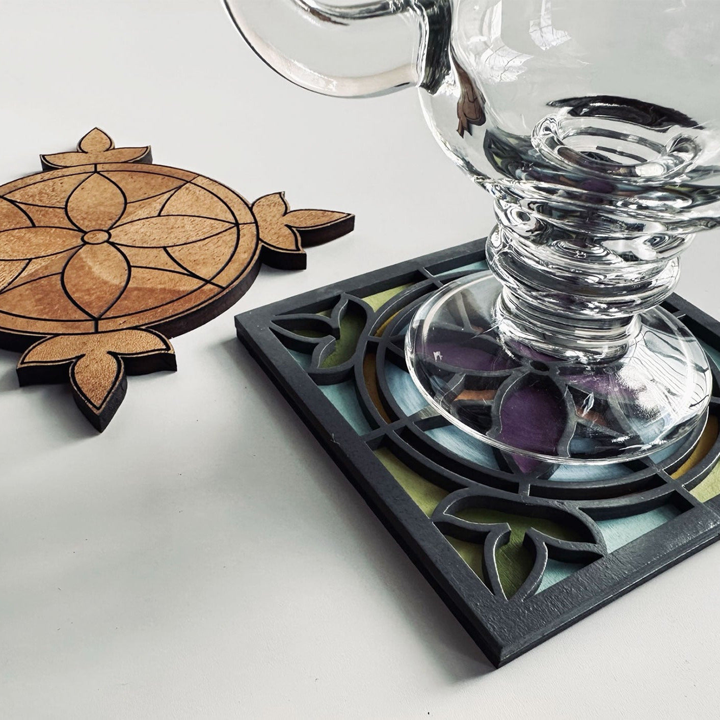 Glass goblet on a decorative coaster with a wooden coaster next to it on a light surface.