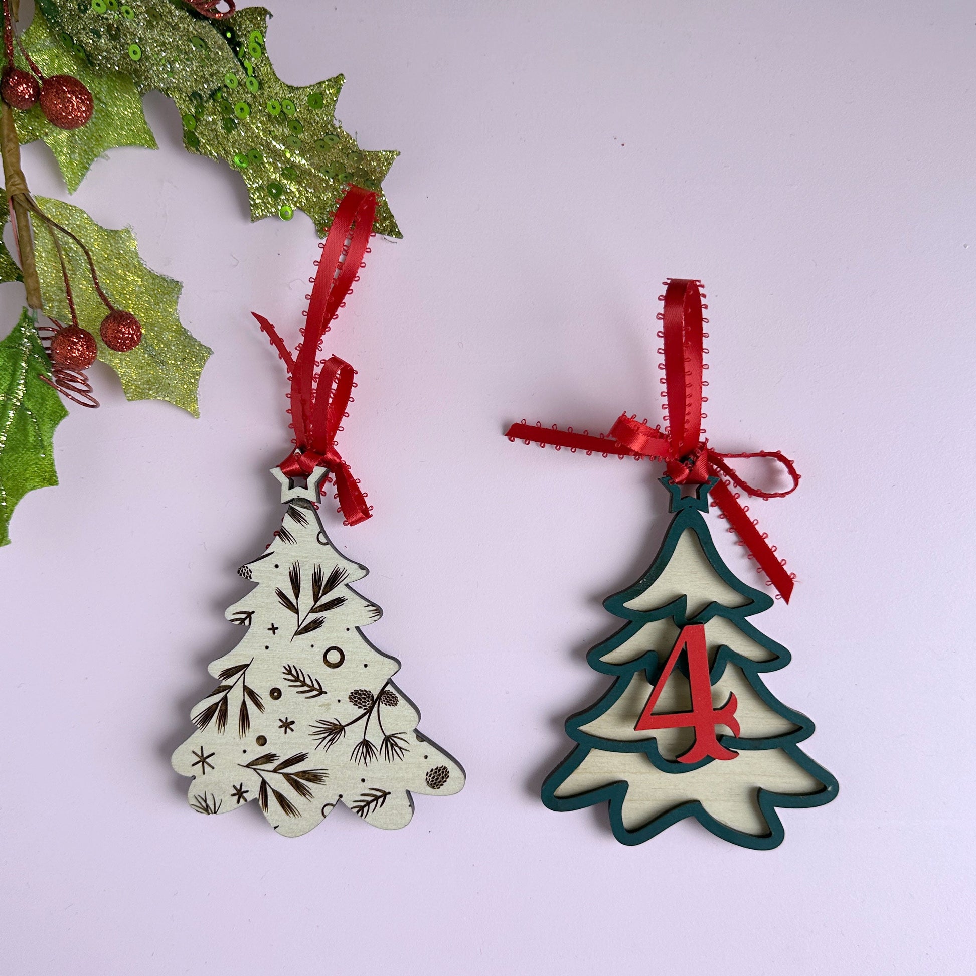 Laser-cut layered Christmas tree ornaments with red ribbon bows, hanging against a holiday backdrop