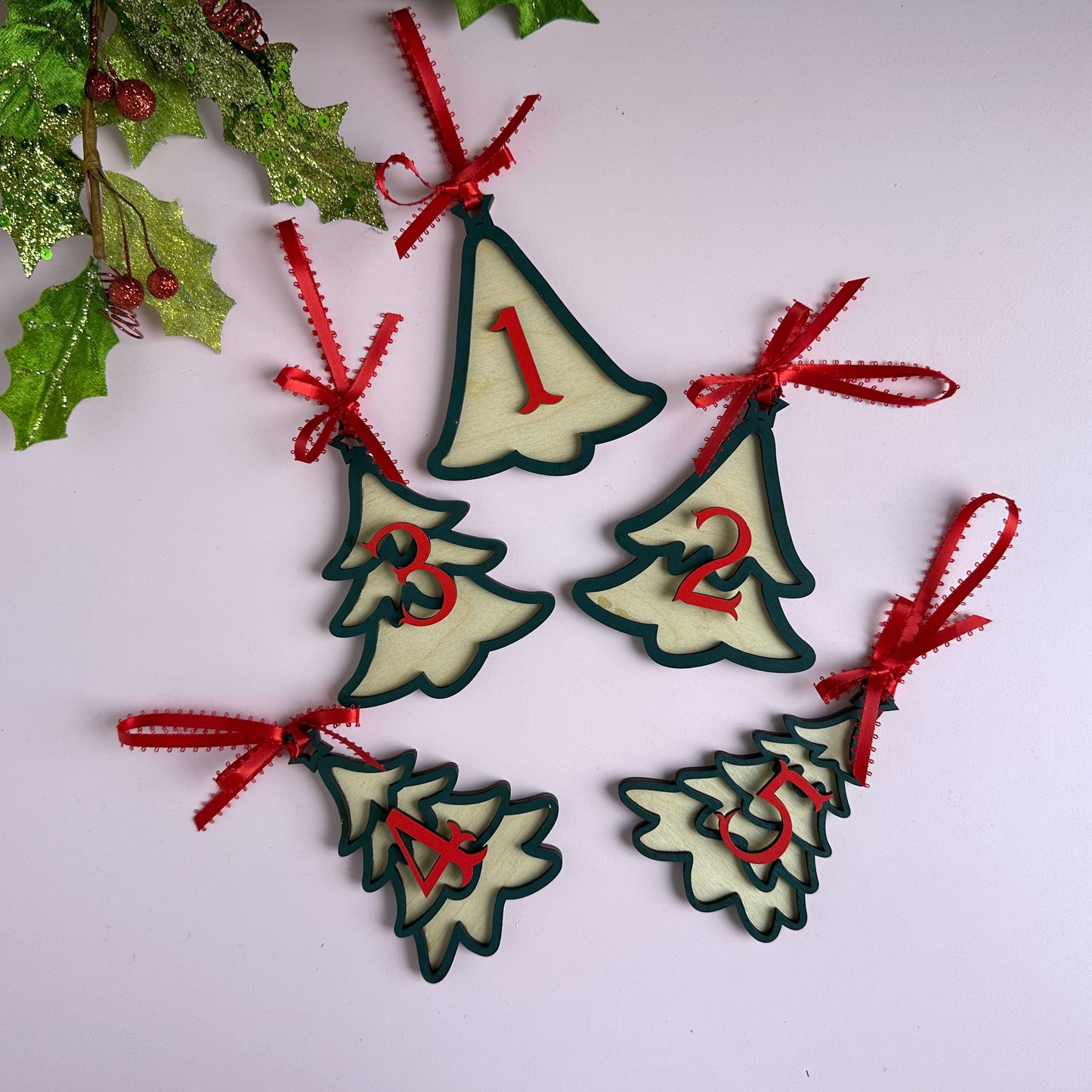 Laser-cut layered Christmas tree ornaments with red ribbon bows, hanging against a holiday backdrop