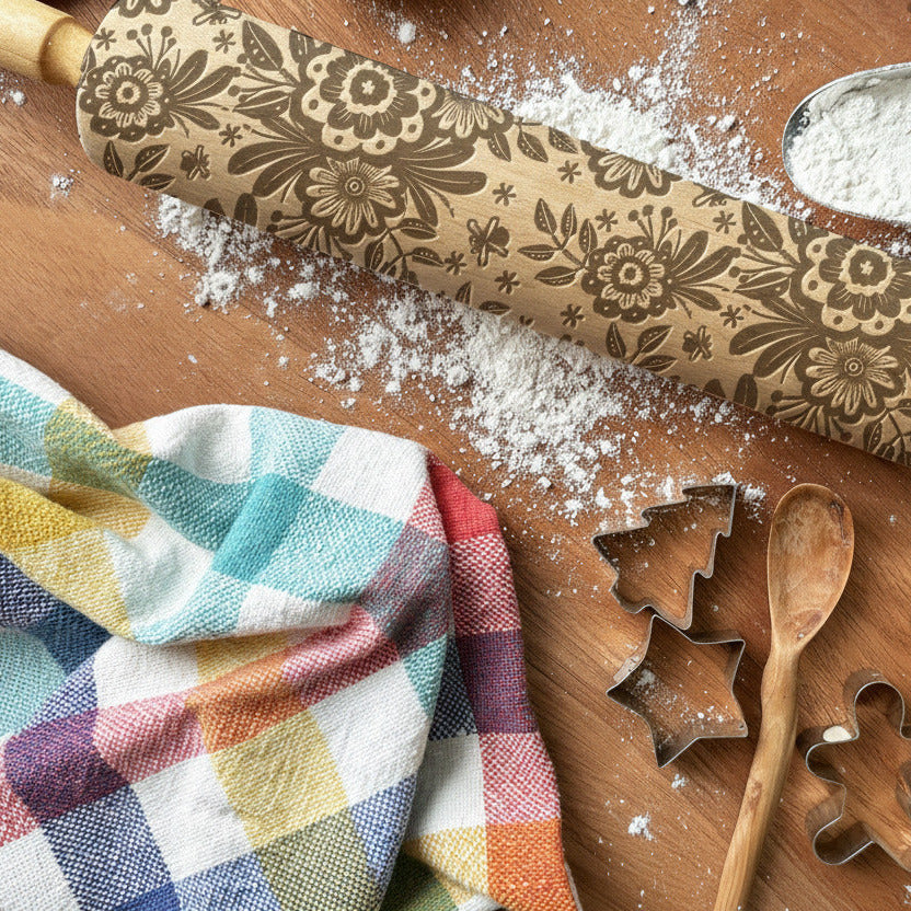 Decorative rolling pin with floral patterns on a wooden surface with baking tools and flour.