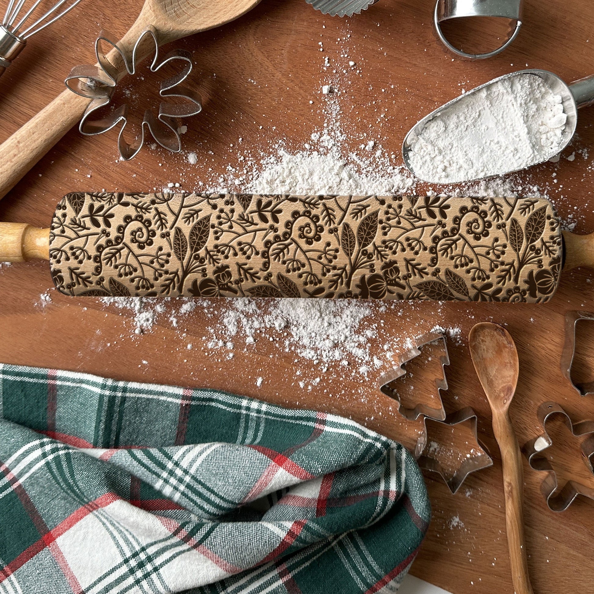 Decorative rolling pin with floral patterns on a wooden surface with flour and kitchen tools.
