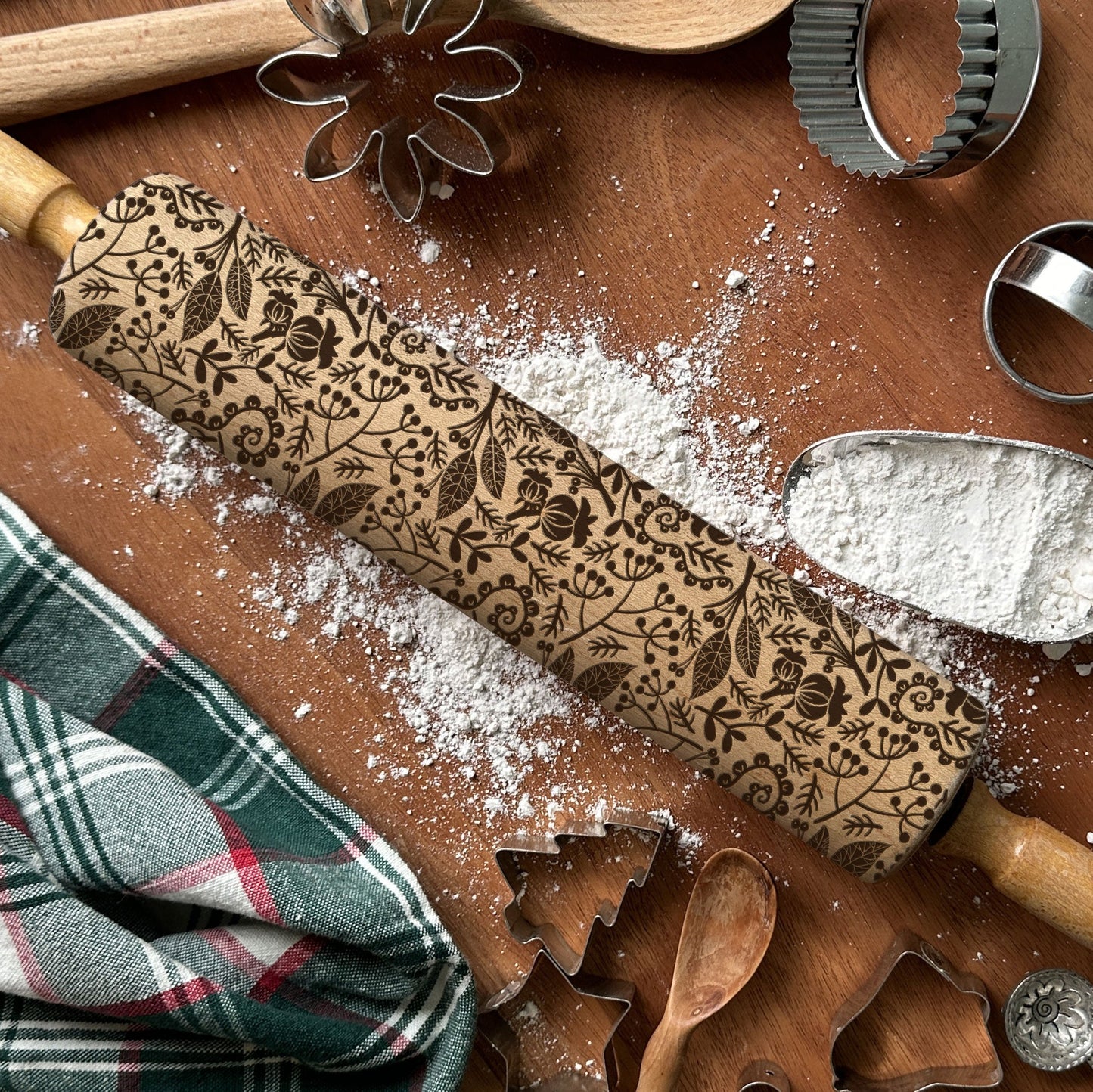 Decorative rolling pin with embossed patterns on a wooden surface with baking tools and flour.